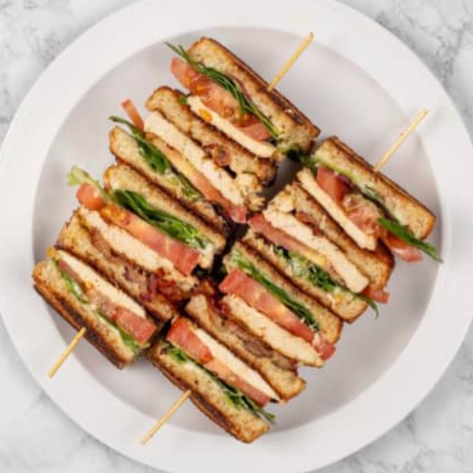 Four club sandwiches, each cut into halves and held together with toothpicks, on a white plate.