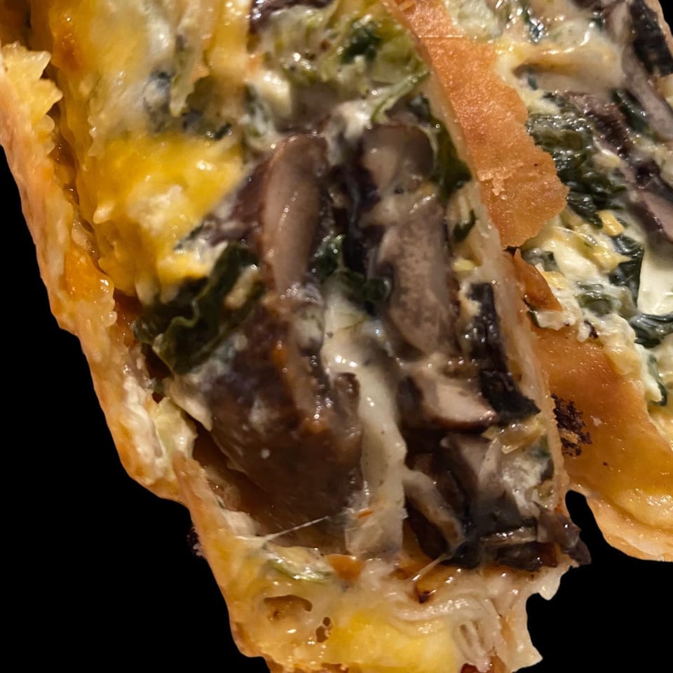 Close-up of a Chef Flavas soul-food dish, showing mushrooms, spinach, and cheese in a pastry.