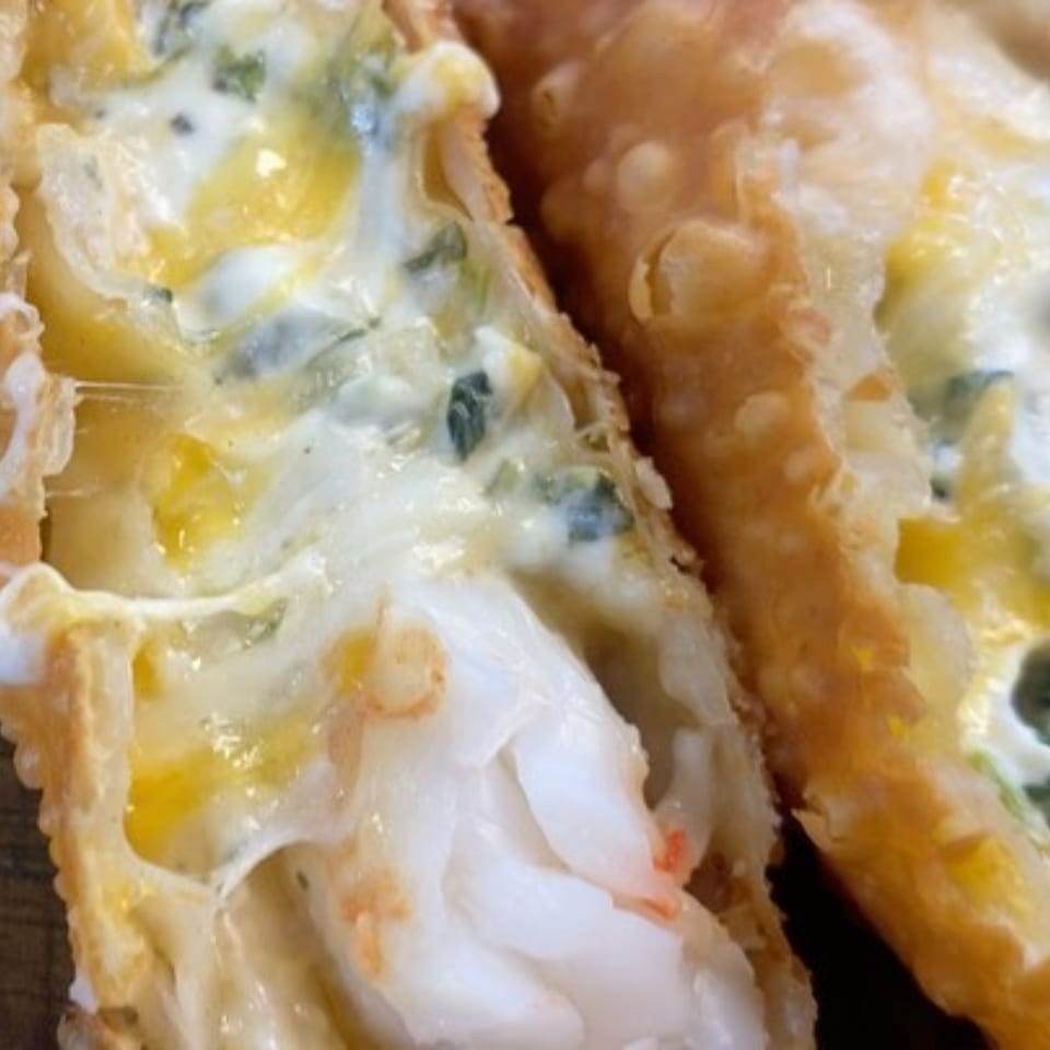 Close-up of a golden-fried pastry, split open to reveal creamy white filling with green specks and shrimp.