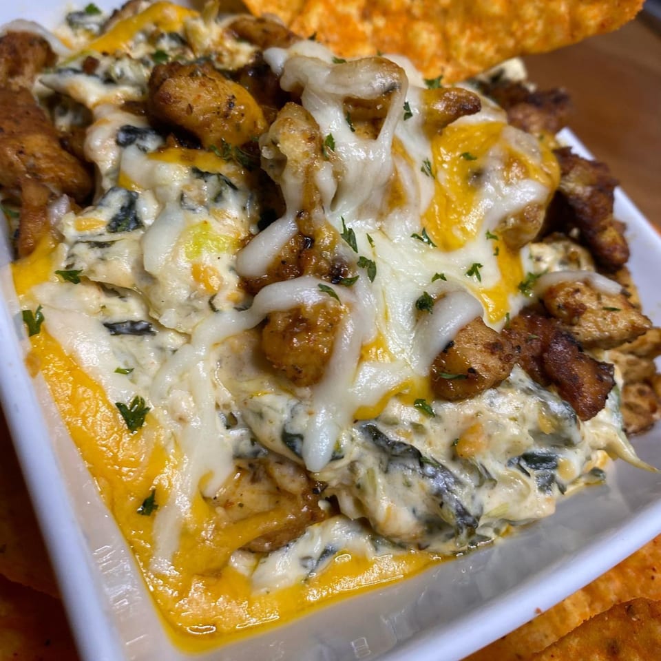 Creamy spinach dip with melted cheese and seasoned chicken pieces, garnished with parsley and tortilla chips.
